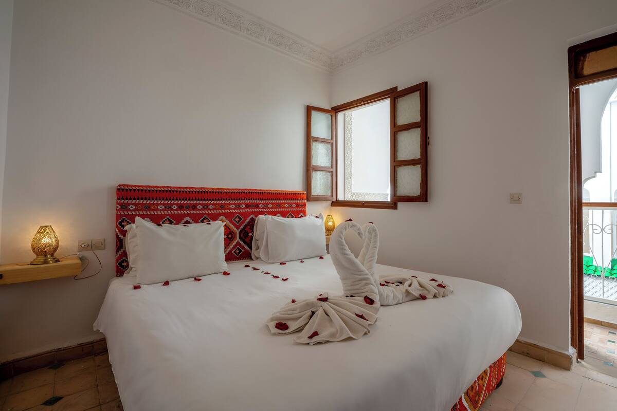 Una cama bien hecha con sábanas blancas y pétalos de rosa roja dispuestos en forma de cisne.