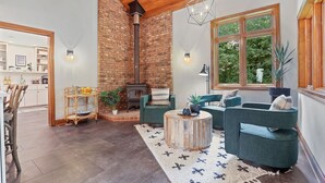 Un salon chaleureux avec une cheminée, des canapés verts, une table basse en bois et une grande fenêtre donnant sur un paysage verdoyant.