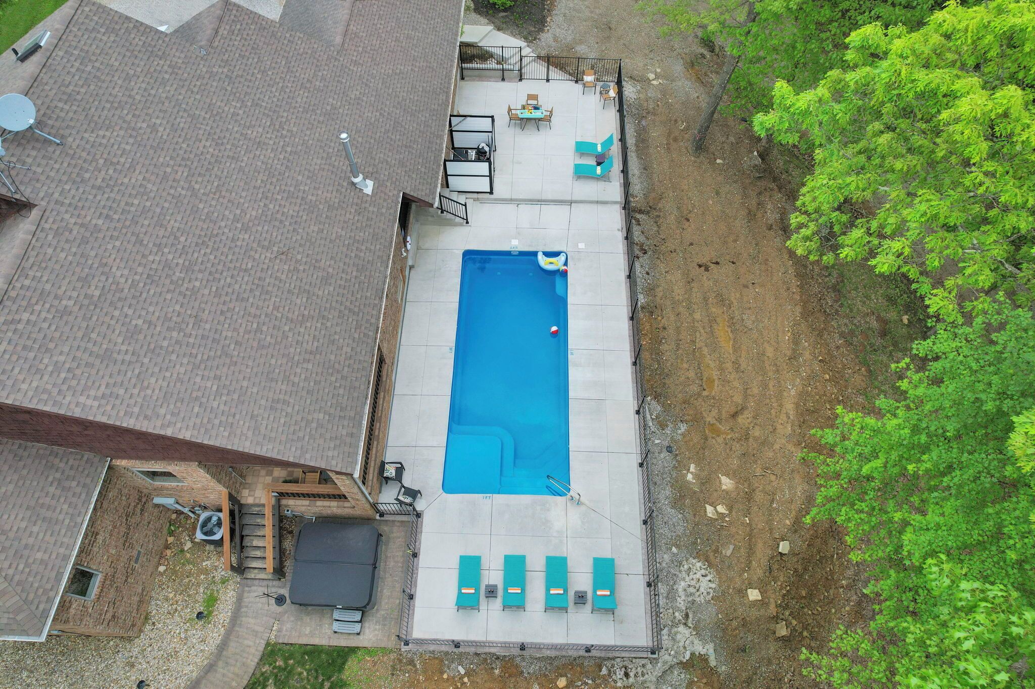 An aerial view of a backyard with a swimming pool, a patio with seating, and a brick house.