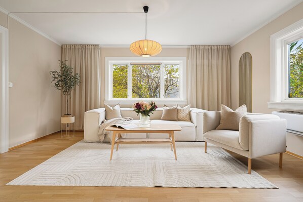Un salon moderne avec un canapé beige, une table basse en bois et une grande fenêtre agrémentée de rideaux.