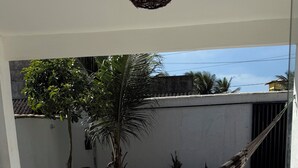 A tiled patio with a hammock, a hanging light fixture, and a view of a building and trees. - Casa Pé na Areia, cozy for guests with good taste. (Praia da Costa Armação dos Búzios)