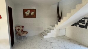 A modern interior with a marble floor, a staircase with a geometric pattern, and a floral chair. - Casa Pé na Areia, cozy for guests with good taste. (Praia da Costa Armação dos Búzios)
