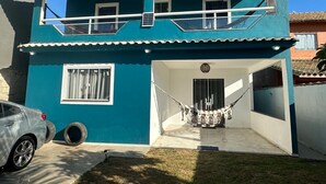 A two-story house with a balcony, a car parked in the driveway, and a hammock in the front yard. - Casa Pé na Areia, cozy for guests with good taste. (Praia da Costa Armação dos Búzios)