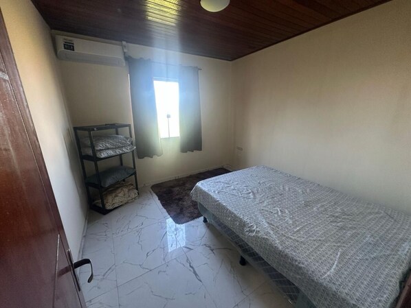 A small, sparsely furnished room with a single bed, a small table, and a window.