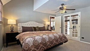 Een slaapkamer met een geborduurde hoofdeinde, een bed met een decoratieve spreideken, twee bedlampen, een plafondventilator en een deur met een ruit.