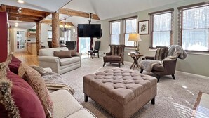 Een ruime woonkamer met een grote televisie, comfortabele zitplaatsen en een open haard.