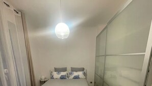 Un dormitorio con cama, mesita de noche, lámpara colgante y puerta corredera de vidrio.
