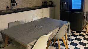 Una cocina moderna con un refrigerador negro, un microondas y una cafetera sobre la encimera. Hay una mesa de comedor con sillas y un salpicadero de baldosas hexagonales.