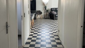Un pasillo con piso a cuadros que conduce a una sala de estar con una televisión de pantalla plana, una lámpara y un sofá.
