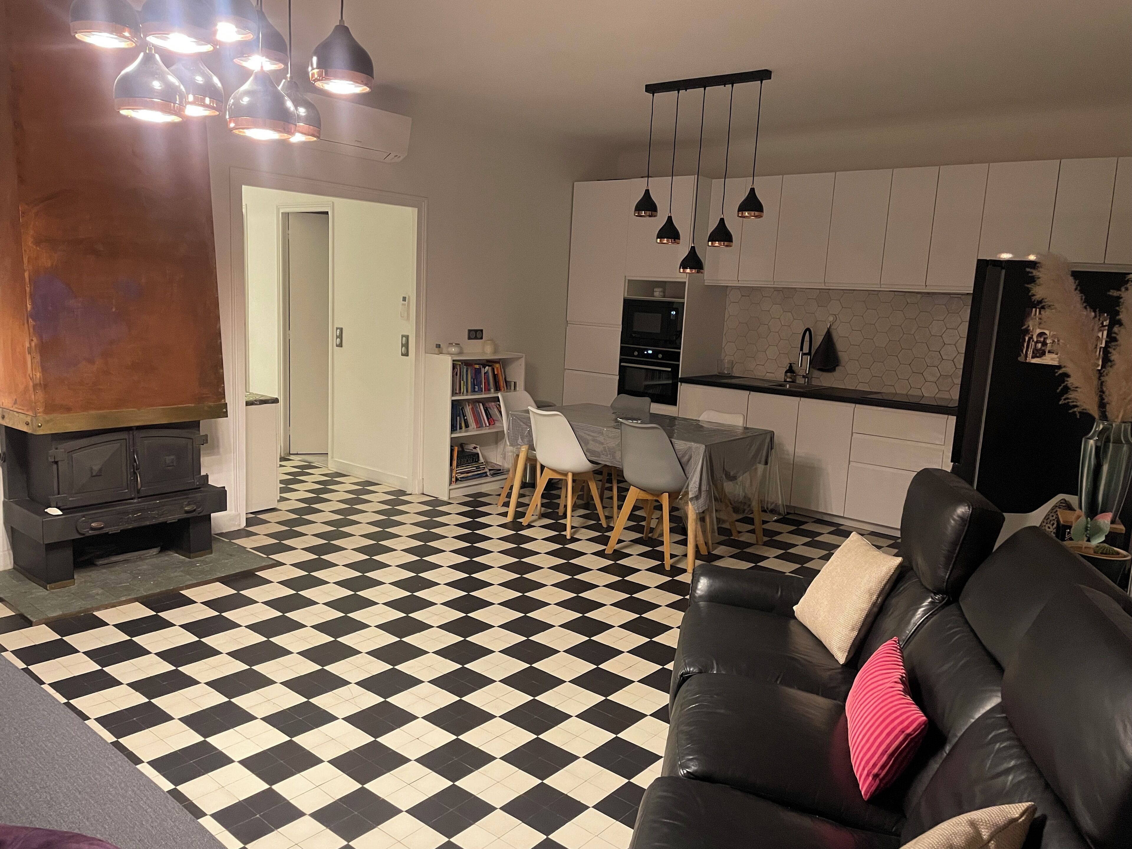 A living room with a black and white checkered floor, a black leather sofa, a dining area with a table and chairs, and a kitchen with white cabinets and a black countertop.