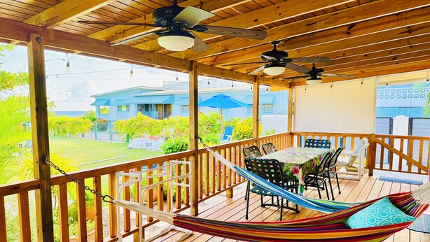 Eine Holzterrasse mit einer Hängematte, einem Tisch mit Stühlen und Deckenventilatoren.