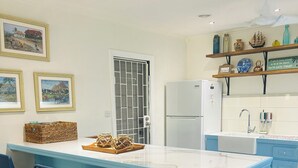 Eine moderne Küche mit einer zentralen Kochinsel, Barhocker, einem Kühlschrank und dekorativen Gegenständen auf Regalen.