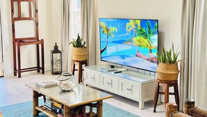 Ein Wohnzimmer mit einem Glastisch, einem Fernseher und zwei Korbwannen mit Pflanzen.