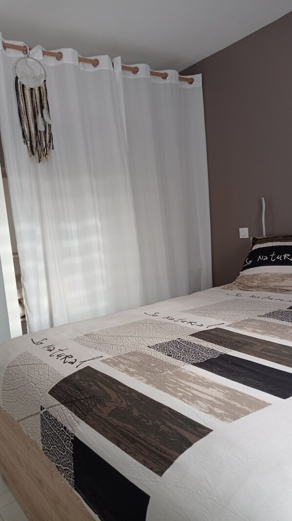 A bedroom with a bed, white curtains, a headboard, and a wall with a light switch. - Quiet house on the island of Oleron (Dolus-d'Oléron)