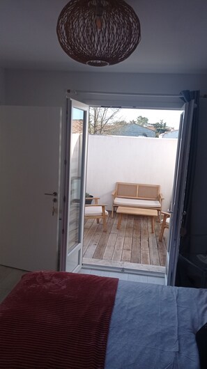 A room with a bed, a wooden bench, and a view of an outdoor area with a wooden deck and a bench. - Quiet house on the island of Oleron (Dolus-d'Oléron)