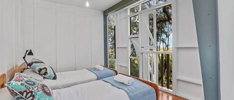 Una camera da letto con due letti, una scrivania e una finestra vista alberi.