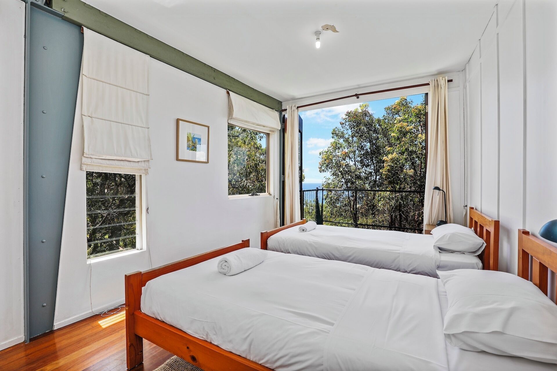 Une chambre avec deux lits, de grandes fenêtres et une vue sur les arbres et la mer.