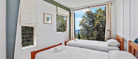 Une chambre avec deux lits, de grandes fenêtres et une vue sur les arbres et la mer.