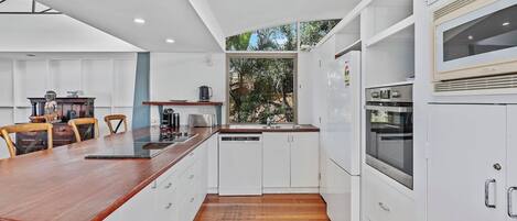 A modern kitchen with white cabinetry, a wooden countertop, and built-in appliances.
