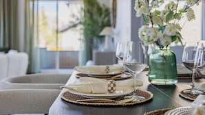 Une table à manger dressée avec de l’assiette blanche, des verres à vin transparents et un vase vert contenant des fleurs blanches.