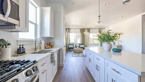 Une cuisine moderne avec des meubles blancs, une cuisinière en acier inoxydable et un grand îlot central agrémenté d’un vase de fleurs.
