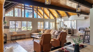 A spacious living area with a high ceiling, large windows, and a cozy seating arrangement. - Spacious 4BR Cabin with a Hot Tub (Munds Park)