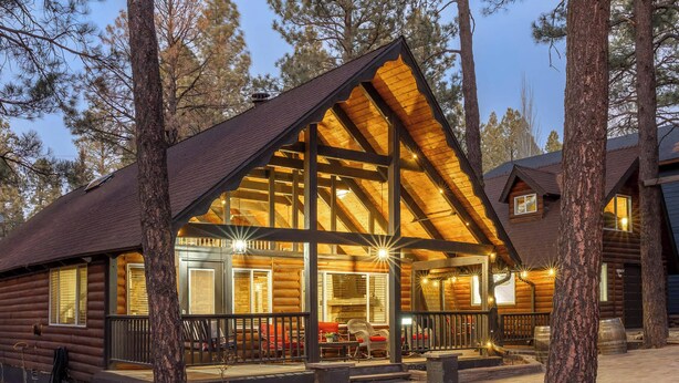 A log cabin with a large porch, multiple windows, and a well-lit interior. - Spacious 4BR Cabin with a Hot Tub (Munds Park)