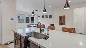 A modern kitchen with a large island, pendant lights, and a dining area with a brick accent wall. - Spacious Pine Retreat with Fire Pit (Flagstaff)
