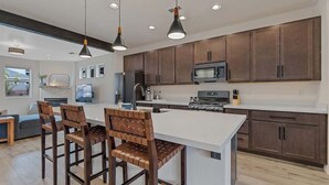 A modern kitchen with dark wooden cabinets, a central island, pendant lighting, and a dining area with wooden chairs. - Spacious Pine Retreat with Fire Pit (Flagstaff)