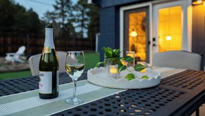 Una botella de vino y dos copas sobre una mesa afuera de una casa con patio.