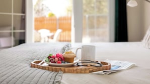 Una cama bien hecha con una bandeja de comida, una taza y vasos sobre una tabla de madera.