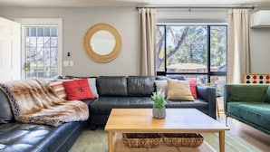 Een woonkamer met een zwarte leren bank, een houten salontafel en een groene fauteuil.