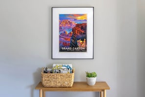 A framed poster of the Grand Canyon National Park on a wall, a woven basket with items on a wooden table below, and a potted plant. - Spacious Forest Retreat w/ A/C near Mountain Park (Flagstaff)