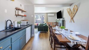Een moderne keuken met een zwart aanrecht, een magnetron en een spoelbak. Er is een eethoek met een houten tafel en stoelen, en een televisie aan de muur bevestigd.