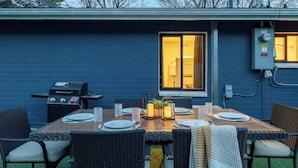 Een terras met een tafel voor vier personen, omringd door rieten stoelen, en een barbecue op de achtergrond.