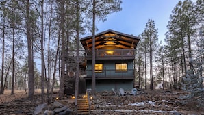 A two-story cabin with a balcony, surrounded by trees and a stone wall. - Arcade Cabin with Forest Views & Hot Tub (Munds Park)