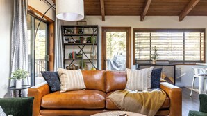 A cozy living room with a brown leather sofa, a wooden coffee table, and a bookshelf filled with books and decorative items. - Arcade Cabin with Forest Views & Hot Tub (Munds Park)