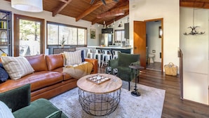 A spacious living room with a leather sofa, a round coffee table, and a chandelier. - Arcade Cabin with Forest Views & Hot Tub (Munds Park)