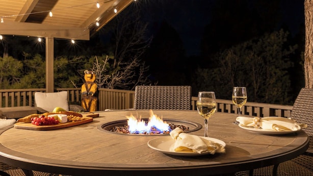 An outdoor dining area with a round table, a fire feature, and string lights. - Arcade Cabin with Forest Views & Hot Tub (Munds Park)