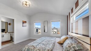 A bedroom with a bed, two windows, a mirror, and a door leading to a bathroom. - Spacious 3BR|2.5Bth | Free parking in Saddle Ridge (Calgary)