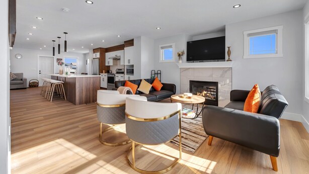 A modern living room with a fireplace, a kitchen in the background, and a dining area with bar stools. - Spacious 3BR|2.5Bth | Free parking in Saddle Ridge (Calgary)