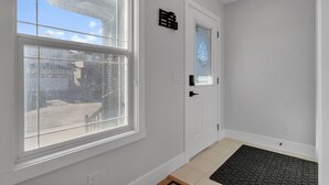 A clean, white-walled hallway with a large window, a door with a frosted glass panel, and a black mat at the entrance. - Spacious 3BR|2.5Bth | Free parking in Saddle Ridge (Calgary)