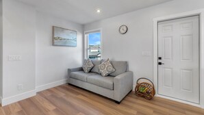 A living room with a grey sofa, a painting on the wall, a clock, and a door. - Spacious 3BR|2.5Bth | Free parking in Saddle Ridge (Calgary)