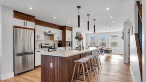 A modern kitchen with a large island, stainless steel appliances, and wooden accents. - Spacious 3BR|2.5Bth | Free parking in Saddle Ridge (Calgary)