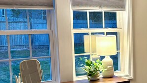 Een slaapkamer met een houten dressoir, een bedlamp, een spiegel en een raam met jaloezieën.