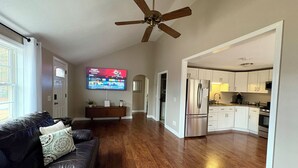 Een ruime woonkamer met een donker leren bank, een plafondventilator en een flatscreen televisie aan de wand.