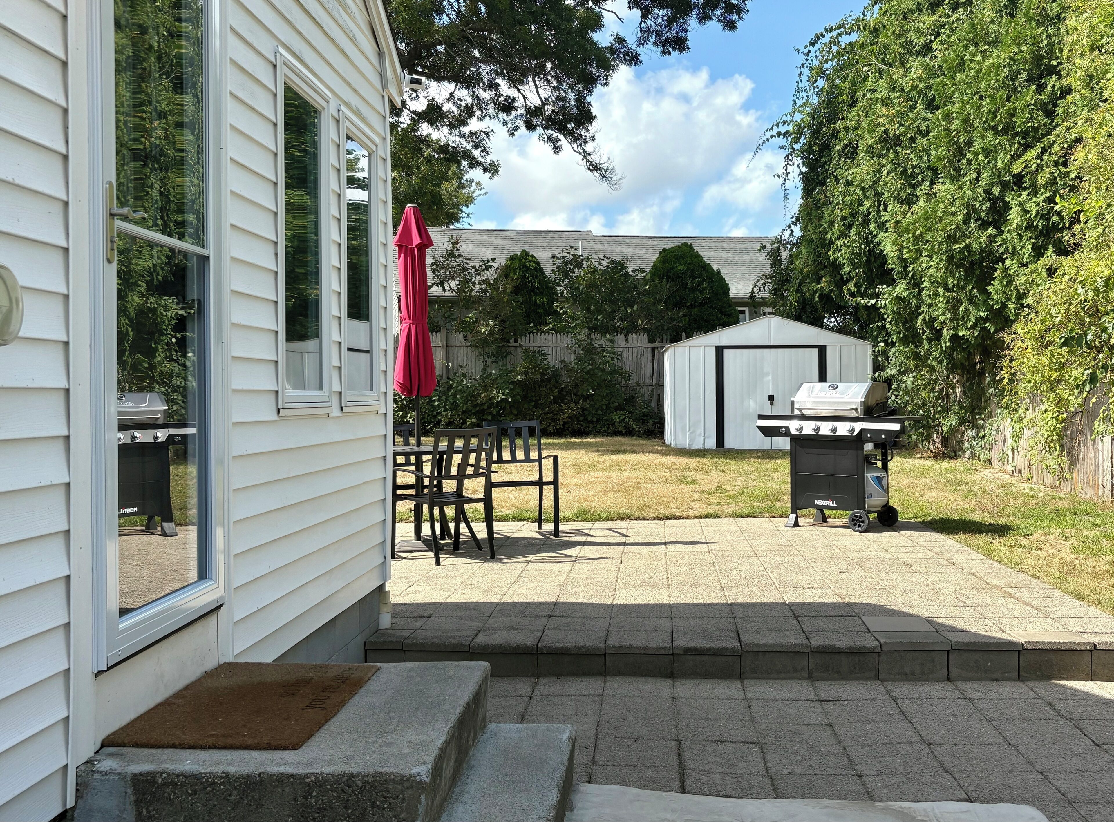 Ein Garten mit Terrasse, Grill und Geräteschuppen.