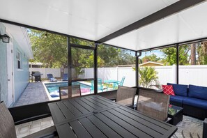 A covered outdoor patio with a pool, seating area, and a table.