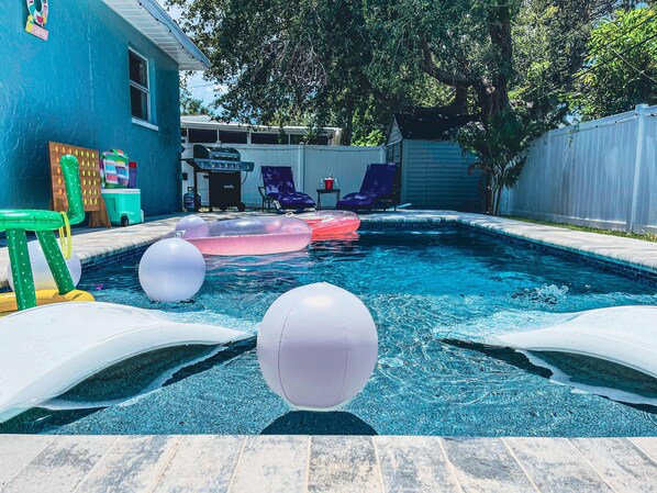 A swimming pool with inflatable toys, a barbecue grill, and outdoor seating.
