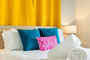 Una cama con cabecera blanca, almohadas blancas y una toalla blanca enrollada.